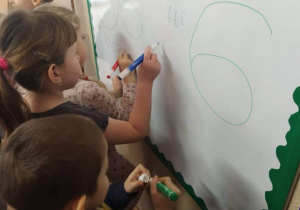 Dzieci piszą cyfrę na tablicy